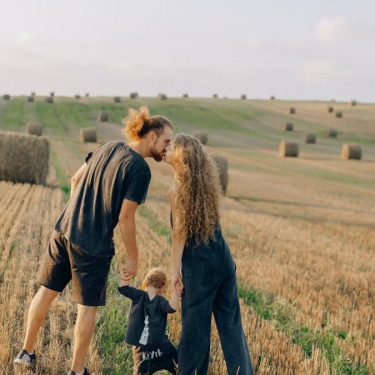 A couple with their child enjoy a sunny day in a wheat field, symbolizing love and joy.